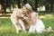 Young girl in white dress and straw hat feeding golden retriever while smiling and sitting on meadow with closed eyes