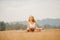 Young girl in white shirt, sportswear with long hair Blonde meditates yoga in field sunrise. Relaxation concept