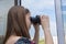 A young girl from the window is watching the street and neighboring houses through binoculars. Concept: spying on neighbors, gathe