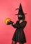 A young girl in a witch hat holds a pumpkin. Wears scary makeup, Halloween or death day, dressed in black clothes