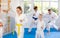 Young girl and woman in kimono and colored belt practicing karate punch block during group martial arts lesson in gym