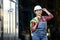 Young girl in a work dress and white hard hat in a factory. Woman in a work uniform holding reflective vest in a storage.