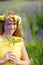 Young girl in yellow dress walking on meadow with lilac lupines. Warm summer day. Flower wreath for head