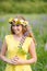 Young girl in yellow dress walking on meadow with lilac lupines. Warm summer day. Flower wreath for head