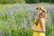 Young girl in yellow dress walking on meadow with lilac lupines. Warm summer day. Flower wreath for head
