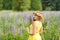 Young girl in yellow dress walking on meadow with lilac lupines. Warm summer day. Flower wreath for head