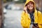 A young girl with yellow raincoat is posing for a photo while walking the city and listening to the music on the rain. Walk, rain