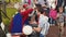 Young girls in clown suits paint face to boy, woman in summer festival. Children