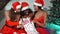 Young girls European, Asian and African in red New Year`s clothes and a hat sit on a bench at a Christmas tree holding a bag of