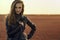 Young glam model with the wind in her long hair wearing black stylish leather jacket standing in the deserted field at sunset