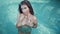 Young glamour woman in bikini standing in the swimming pool on villa and looking at the camera