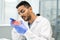 Young gloved scientific researcher in whitecoat looking at meat in petri dish