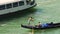 Young gondolier rowing boat with passenger on hot summer day, ferry passing by