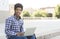 Young good-looking student sitting with laptop against cityscape