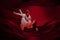 Young and graceful ballet dancers on billowing red cloth background in classic action. Art, motion, action, flexibility