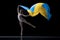 Young graceful classic ballerina dancing with cloth painted in blue and yellow colors of Ukraine flag on dark studio