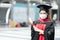 Young graduated Asian woman wear black gown, cap with red tassels and face mask holding diploma after graduation.