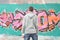 A young graffiti artist in a gray hoodie looks at the wall with