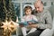 Young grandfather play and read book with her adorable grandaugher nea fir tree. Christmas mood