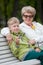 Young grandson showing new spinner gadget, happy senior grandma hugging boy on bench in park at day