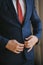 A young groom man businessman in a blue suit and a red tie button his jacket