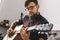 Young guitarist hipster at home with guitar sitting playing concentrated close-up