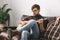 Young guitarist hipster at home with guitar sitting playing relaxed close-up