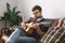 Young guitarist hipster at home with guitar sitting wearing eyeglasses playing