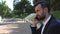 Young guy businessman with a beard holds a phone near his ear, sitting on a park bench. Bearded man in a classic suit. Business