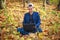 Young guy businessman in classic blue jacket with laptop sitting in forest park in autumn