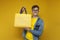 Young guy buyer holds a yellow eco package in his hands and smiles on a yellow background