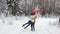 A young guy is circling his beloved girl in the snow forest, they are holding heart-shaped balloons in their hands.