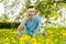 Young guy communicates on a smartphone and sitting on green grass with dandelions on a background of trees