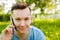 Young guy communicates on a smartphone and sitting on green grass with dandelions on a background of trees