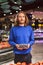 Young guy in dark blue sweater dreamily looking in camera while holding blueberries in hand in modern supermarket