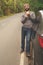 Young guy eating a burger near a car on an empty road. Food on the trip. Food on the go. Autumn travel. Fast food.