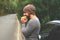 Young guy eating a burger near a car on an empty road. Food on the trip. Food on the go. Autumn travel. Fast food.