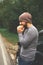 Young guy eating a burger near a car on an empty road. Food on the trip. Food on the go. Autumn travel. Fast food.