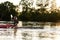 Young guy holding a paddle while boating on a lake surrounded by peaceful nature at sunset