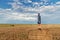 A young guy in a hood stands on a haystack in a wheat field after a rain with a storm sky on the background