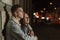 Young guy hugs his beloved on night city background. Beautiful young couple on evening romantic date