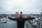 A young guy look at city from the roof of building with his arms raised. Black jacket and orange cap. Belgium, Antwerp.