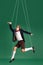 Young guy, marionette on string in motion against green studio background. Puppet. Pressure and manipulation