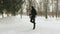 Young guy in a mask on his face, in a black sports suit, performing exercises, jumping rope in a snow-covered Park