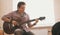 Young guy musician composes music on the guitar and plays in the kitchen, close up