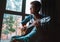 Young guy plaing on guitar and sits near the window