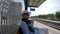 A young guy in a scarf and hat smokes while waiting for a train at the station of Calella, Spain