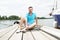 A young guy sits in blue polo on pier near the yacht. happy smiled tourist handsome man relaxing and enjoying the view on river.