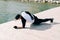 A young guy in sports black clothes on a pier near the lake doing sports exercises in the plank on a Sunny spring day, healthy