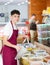 Young guy in supermarket, scooping marinated olives from bucket with ladle